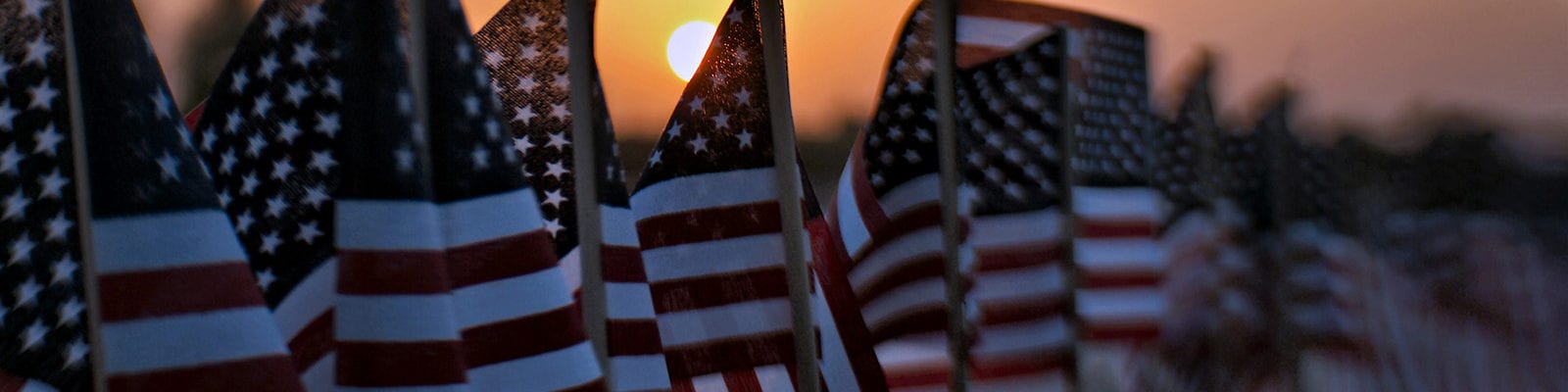 A sunset settling behind a row of small, toy American flags.