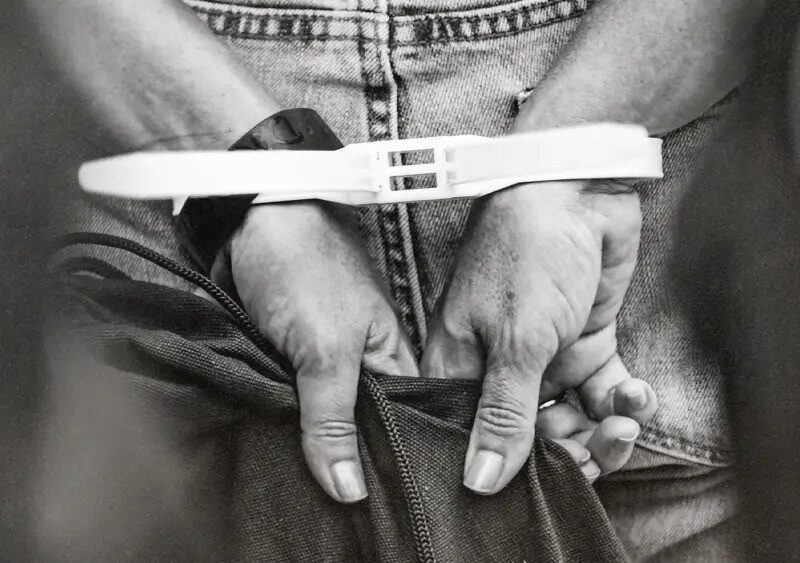 An individual with their hands handcuffed behind their back.